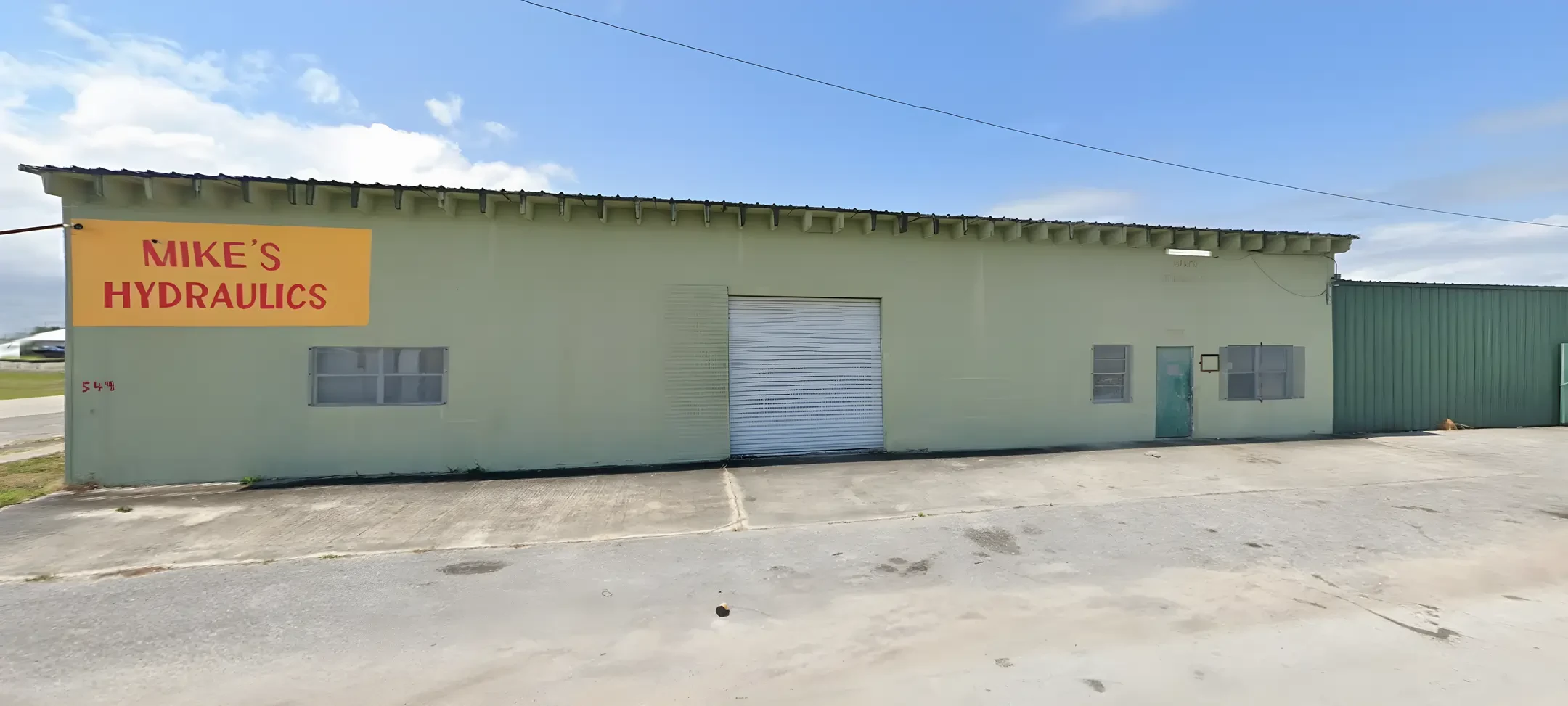The Mike's Hydraulics shop: a long green building with the yellow sign on the wall and a white roll-up door
